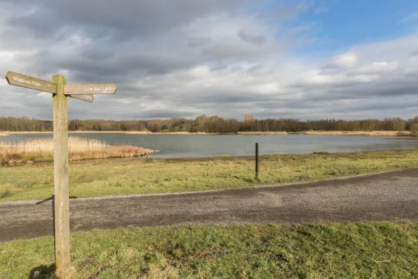 Amberswood Lake today. A wooden signpost pointing towards a large lake with woodland in the distance